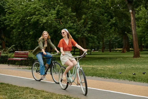 stock image A young lesbian couple rides bicycles in a green park, enjoying a sunny afternoon.