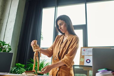 A young woman with long brunette hair is standing in an office, adjusting a wooden figurine. clipart