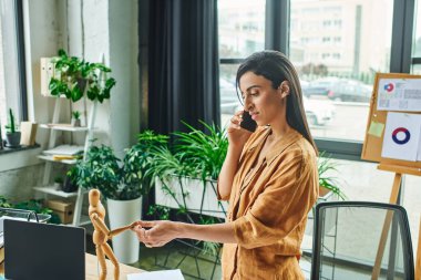 Esmer saçlı güzel bir Orta Doğulu kadın modern bir ofiste çalışıyor, masasında dururken telefonla konuşuyor..
