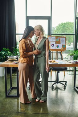 Two young women in smart casual attire stand close together in a modern workspace, sharing an intimate moment amidst their work clipart