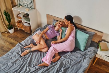 Lezbiyen bir çift pijamalarıyla bir yatağa kıvrılır, birlikte güzel bir anın tadını çıkarırlar..