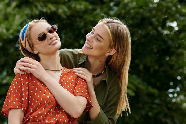 Two women embrace in a green park, sharing a smile on a sunny day.