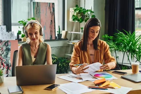 stock image Two women in a modern office setting work on a project together, focusing on their tasks.