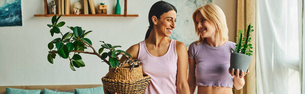 Две женщины, одна темноволосая и одна блондинка, обнимаются и улыбаются в своем доме, излучая вместе счастье