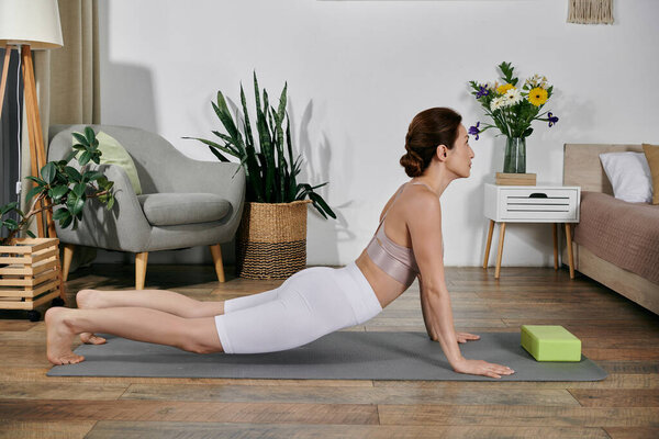 A woman in a crop top performs a yoga pose on a mat in a modern apartment.
