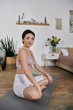 Ekin bluzlu ve şortlu Asyalı kadın modern, iyi ışıklandırılmış odada yoga minderi üzerinde meditasyon yapıyor.