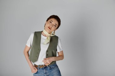 Yeşil yelekli, beyaz tişörtlü, kısa siyah saçlı, gülümseyen ve yan tarafa bakan kendine güvenen Asyalı kadın.