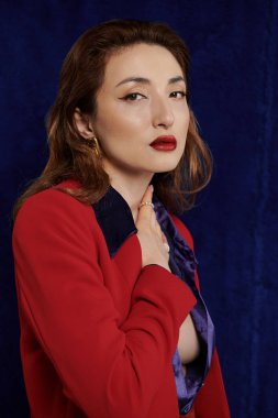 Çekici bir Asyalı kadın koyu bir arka plana karşı kırmızı bir takım elbise ve ipek gömlek içinde poz veriyor, kendine güveni ve tarzı var..