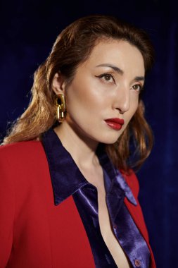 Şık bir Asyalı kadın kırmızı takım elbise ve ipek gömlekle poz veriyor. Kendine güvenen bir ifade ve gizem dolu bir ifade..