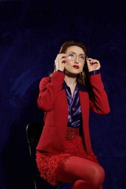 Kırmızı elbiseli bir kadın, gözlerini dikmiş, karanlık bir arkaplana bakıyor, büyüleyici bir görüntü yaratıyor.