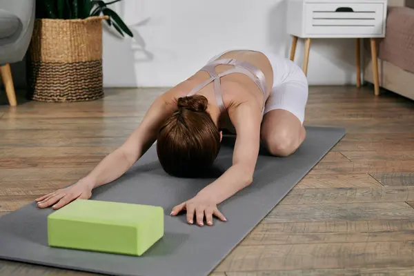 stock image An Asian woman in a crop top practices yoga and meditation on a mat in her modern apartment.