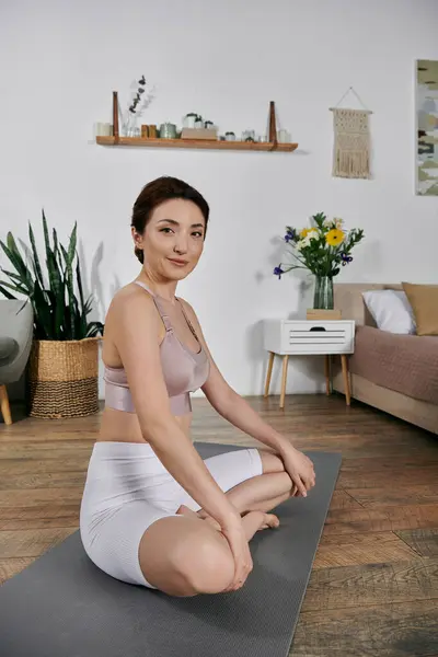 stock image Asian woman in crop top and shorts meditates on yoga mat in modern, well-lit room