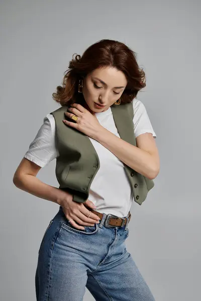 stock image A stylish Asian woman poses in a green vest, a white t-shirt, and blue jeans against a gray background.