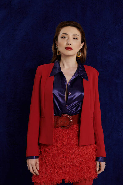 Азиатка в красном костюме уверенно позирует на темно-синем фоне, создавая поразительное изображение