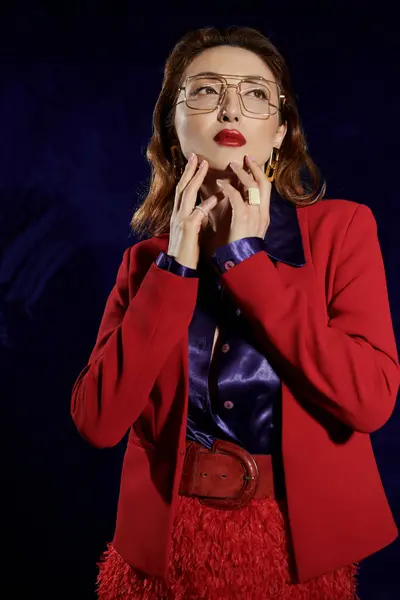 stock image A woman in a red suit with a silk shirt poses confidently against a dark background.