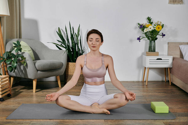 Женщина в топе практикует йогу и медитацию в своем доме, окруженная растениями и успокаивающим декором.