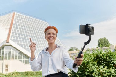 Beyaz tişörtlü bir kadın selfie çubuğuyla bir video kaydediyor..