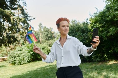 Elinde gurur bayrağı olan bir öğretmen kampüste selfie çekiyor..