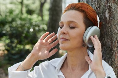 A teacher with red hair listens to music with her eyes closed. clipart