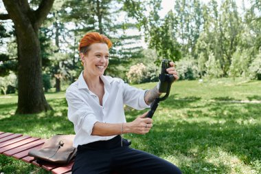 A woman smiles as she films herself with a smartphone on a tripod. clipart