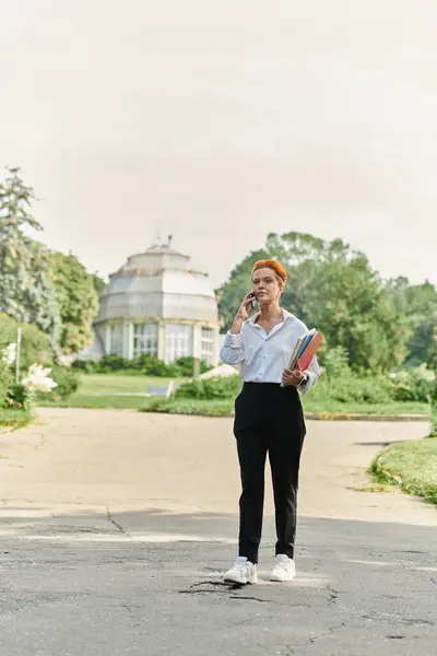 stock image A teacher walks through a campus, talking on her phone and carrying books.