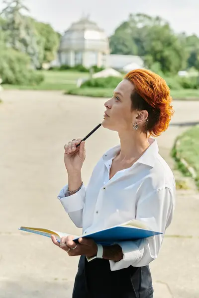 stock image A woman in a white shirt, holding a notebook and a pen, looks up and contemplates on a sunny day.