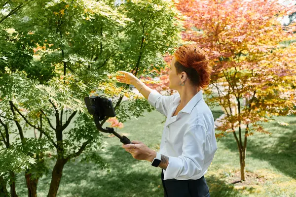 stock image On campus, a teacher reaches for a tree, capturing the moment on her phone