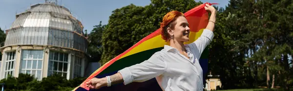 stock image A woman stands outdoors, holding a rainbow flag high in the air, on a university campus.