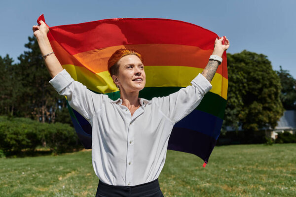 A young woman holds a rainbow flag high, celebrating pride on a sunny day.
