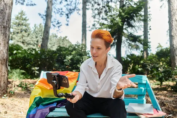 stock image teacher with red hair sits on bench, recording video lesson on smartphone