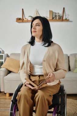 Tekerlekli sandalyede oturan bir kadın elinde bir kitapla pencereden dışarı bakıyor..