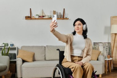 Tekerlekli sandalyedeki bir kadın oturma odasında selfie çekerken gülümsüyor..