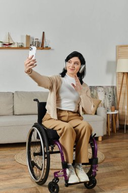 Tekerlekli sandalyedeki bir kadın gülümserken ve kulaklık takarken selfie çeker..