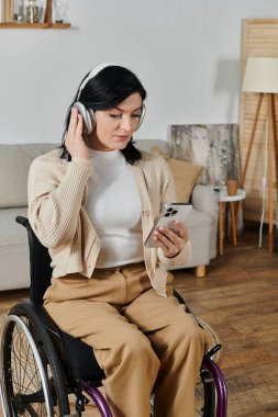 Tekerlekli sandalyedeki kadın müzik dinler ve telefonunu kontrol eder.