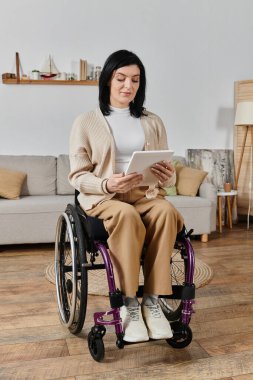 Oturma odasında tekerlekli sandalyede oturan bir kadın tablet kullanıyor..