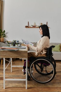 A woman in a wheelchair sits at a desk reviewing documents, focusing intently on the pages. clipart