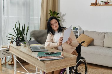 A woman sits in a wheelchair, working at a desk in her home, reviewing a document. clipart