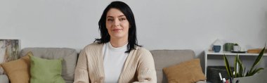 Oturma odasındaki kanepede otururken siyah saçlı bir kadın gülümsüyor..