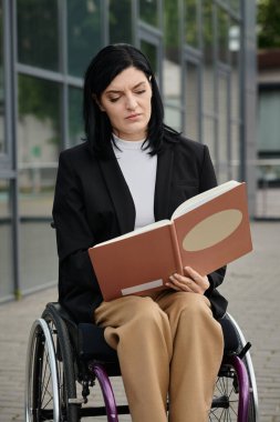 Tekerlekli sandalyedeki bir kadın dışarıda bir kitap okuyor, sayfalarda kaybolmuş..