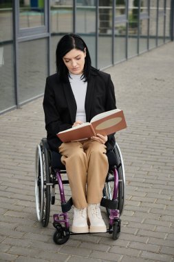 Tekerlekli sandalyede oturan bir kadın dışarıda kitap okuyor..