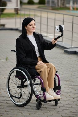 Bir kadın tekerlekli sandalyede selfie çekerken gülümser..