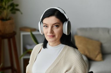 A woman in a wheelchair sits indoors, wearing headphones and listening to music. clipart