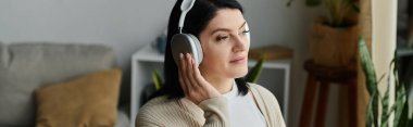 Tekerlekli sandalyede oturan bir kadın oturma odasında kulaklık takıp müzik dinliyor..