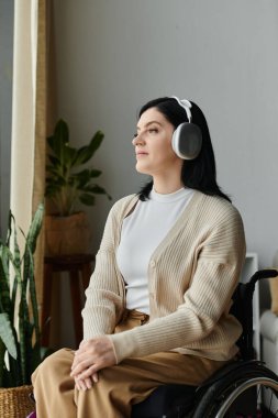 Tekerlekli sandalyedeki bir kadın kulaklıkla müzik dinliyor, pencereden dışarı bakıyor..