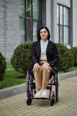 Tekerlekli sandalyedeki bir kadın şehrin kaldırımında güven içinde oturur..