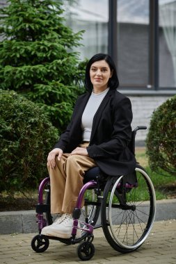 Tekerlekli sandalyedeki bir kadın dışarıya güvenle gülümsüyor..