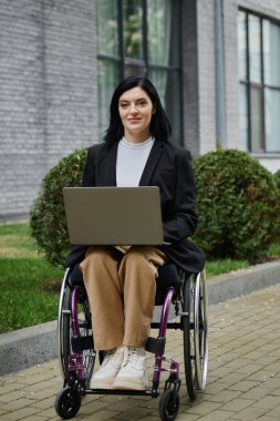 Tekerlekli sandalyedeki bir kadın dizüstü bilgisayarını tuğla bir yolda kullanıyor..