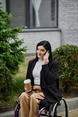Tekerlekli sandalyede oturan bir kadın telefonda konuşuyor ve elinde kahve fincanı tutuyor..