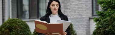 Tekerlekli sandalyedeki bir kadın binanın önünde otururken kitap okuyor..