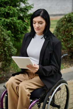 Tekerlekli sandalyedeki bir kadın tabletine odaklanıyor, düşüncelere dalmış..